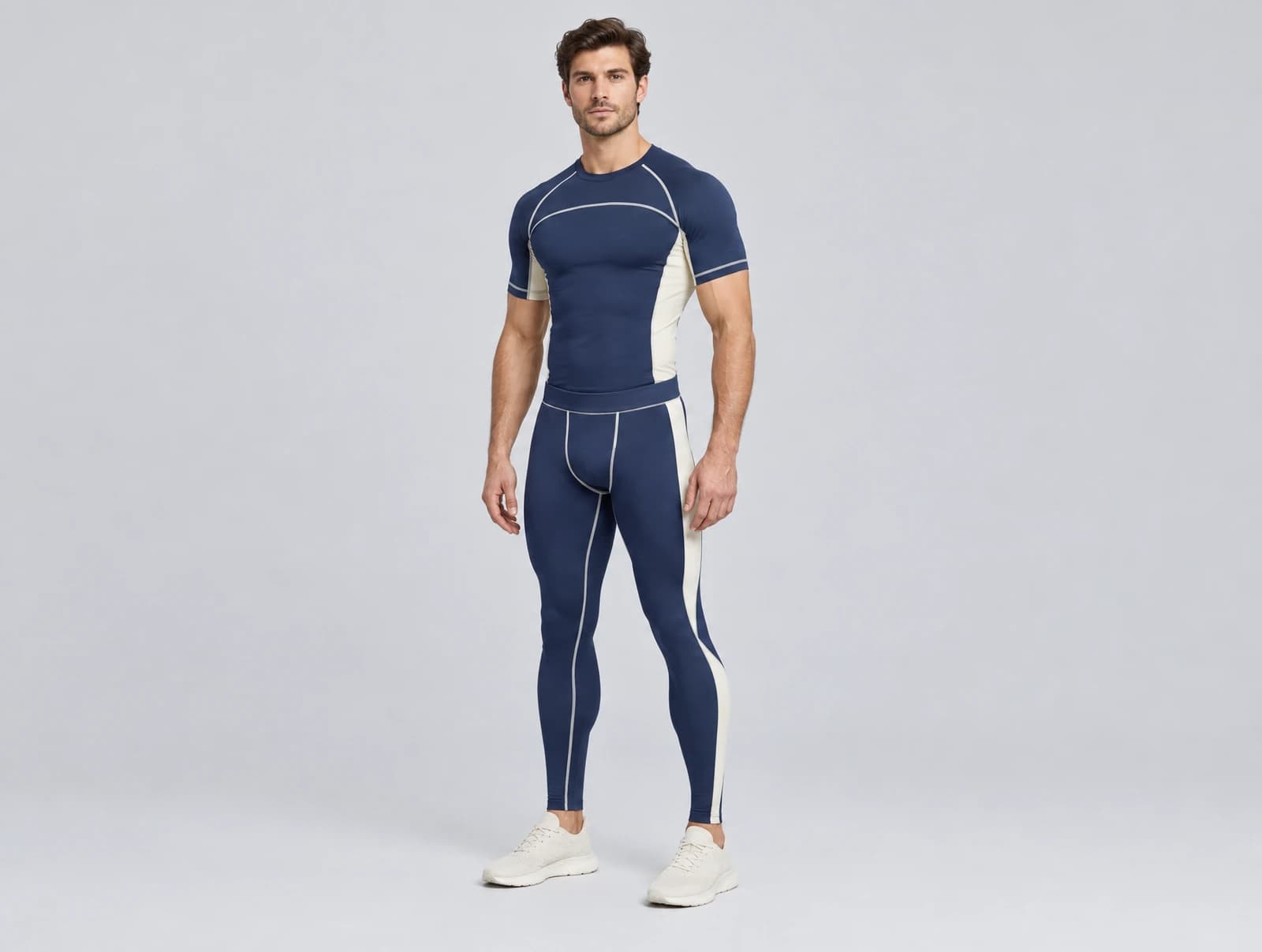 One adult standing in a studio wearing a navy and cream short-sleeve compression top with visible flatlock seams and matching full-length compression tights