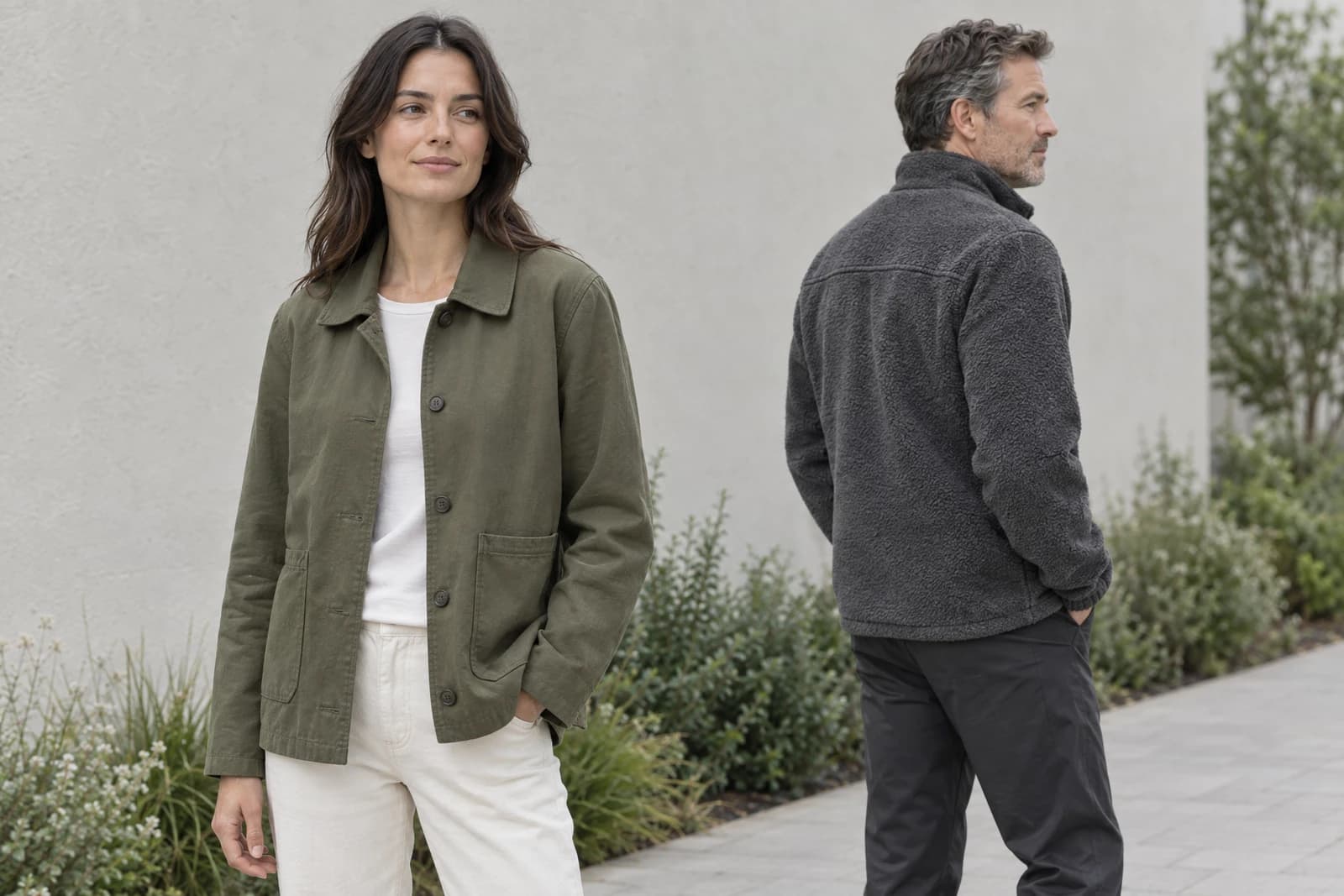 Two adults outdoors wearing an unbranded olive woven chore jacket and a charcoal high-pile fleece jacket seen from the rear