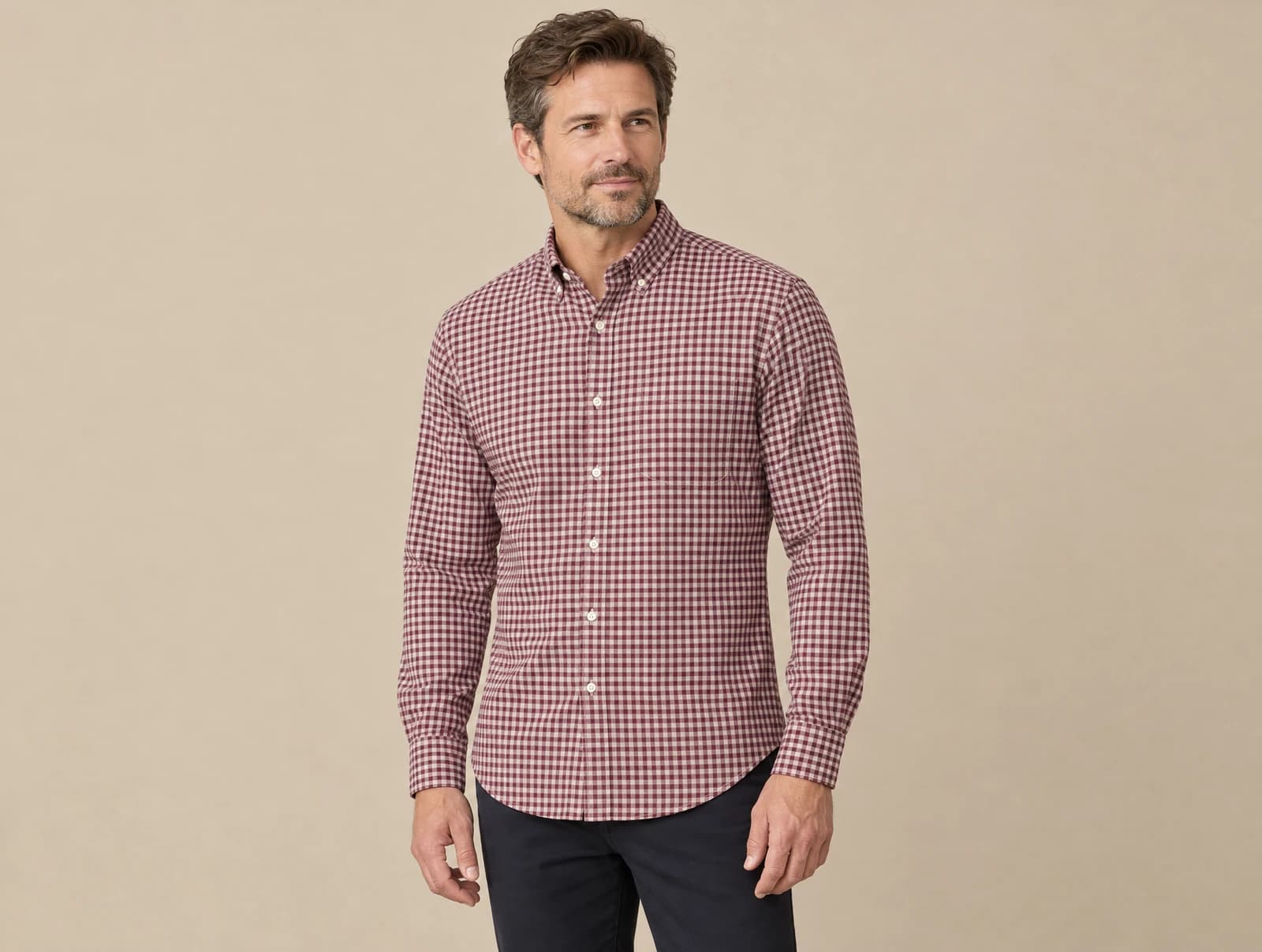 One adult standing in a studio wearing a burgundy and white checked button-down shirt with a chest pocket, worn untucked over navy trousers